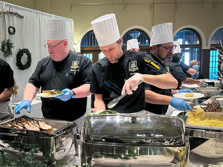 Two male chefs wearing black coats and white toques cook live before the LWTC audience